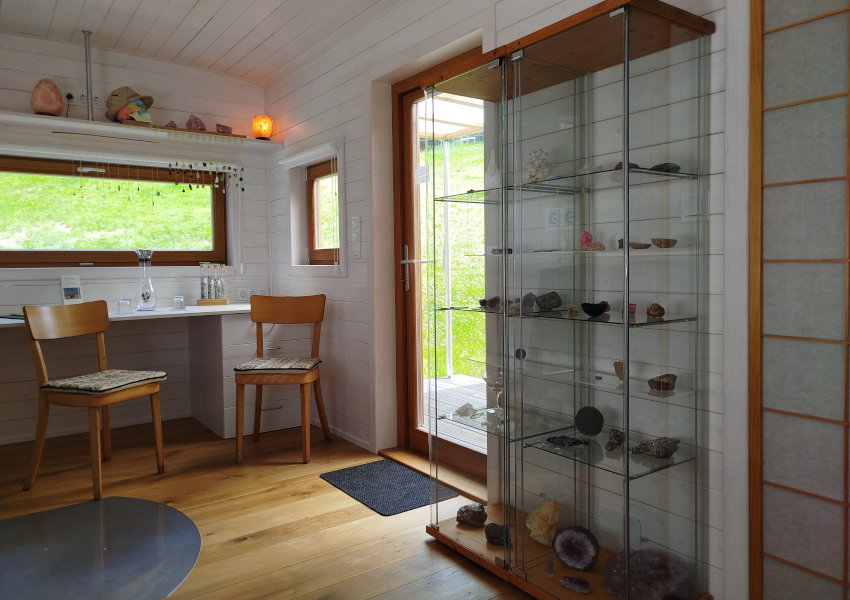 Blick in einen hellen freundlichen Raum.  Es gibt eine Glasvitrine, in der Edelsteine zu sehen sind. Man sieht auch zwei St&uuml;hle und einen Tisch.