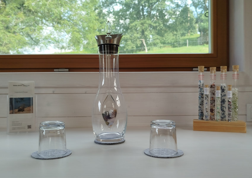 Detailaufnahme: Eine VitaJuwel Glaskaraffe mit Edelsteinen und zwei Trinkgl&auml;ser.